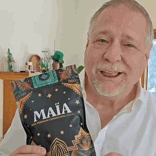 Man holding a bag of MAIA ceremonial cacao, smiling indoors.